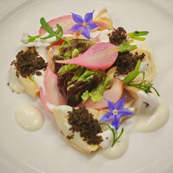 Assiette artistique avec fleurs bleues, légumes colorés et crème blanche.