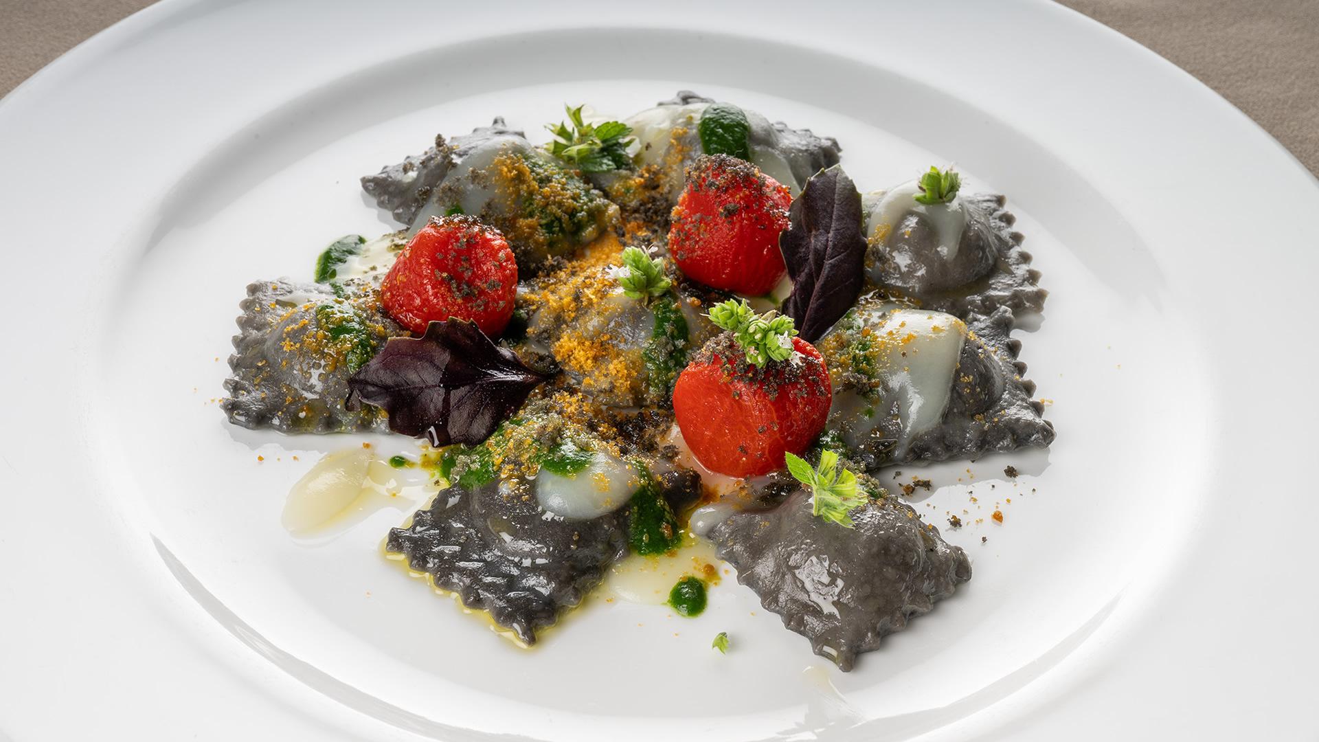 Ravioli neri decorati con pomodorini e foglie, un'esplosione di colori e sapori.