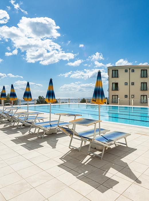Piscina soleggiata, cielo azzurro, relax totale con sdraio e ombrelloni.