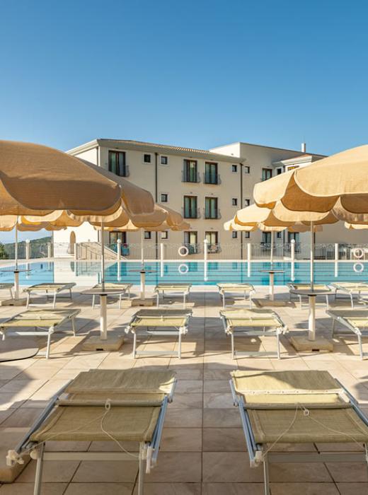 Piscina soleggiata, cielo azzurro, relax totale con sdraio e ombrelloni.