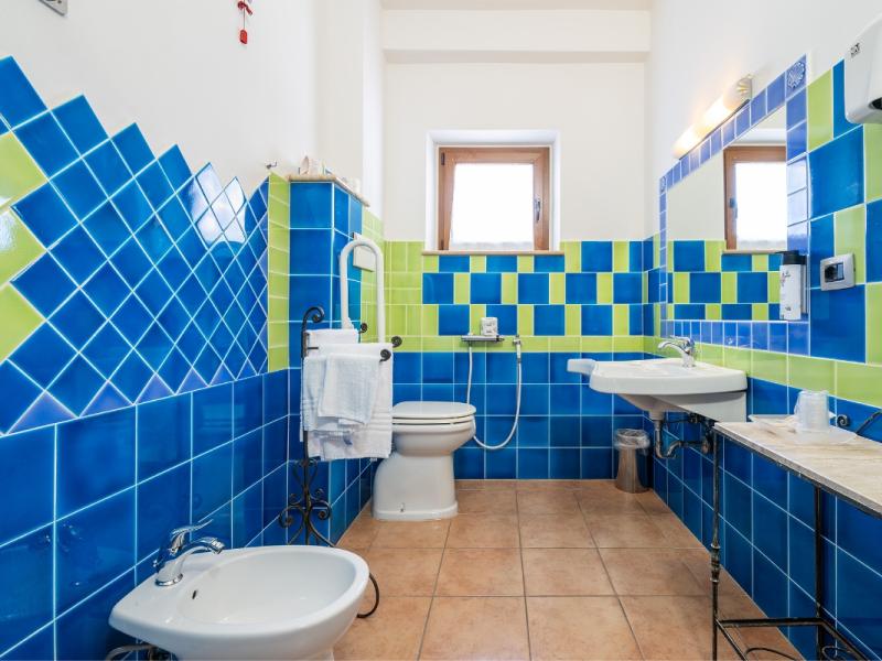 Un bagno con piastrelle blu e verdi sulle pareti con linee pulite e funzionali.