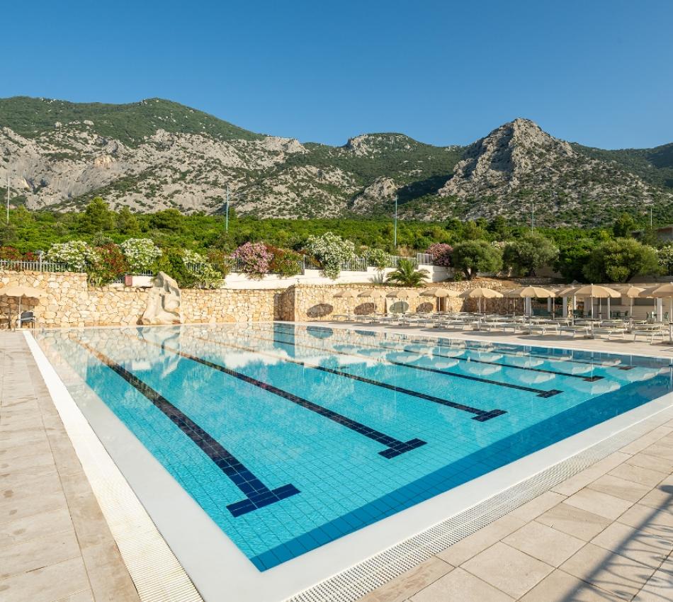 Una piscina vuota con le montagne sullo sfondo con dettagli verdi e curati.